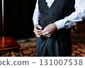 Groom buttoning his classic black vest before the wedding ceremony in elegant setting 131007538