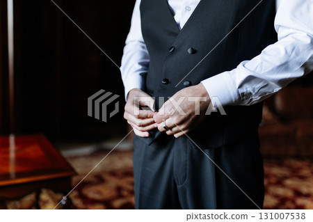 Groom buttoning his classic black vest before the wedding ceremony in elegant setting 131007538