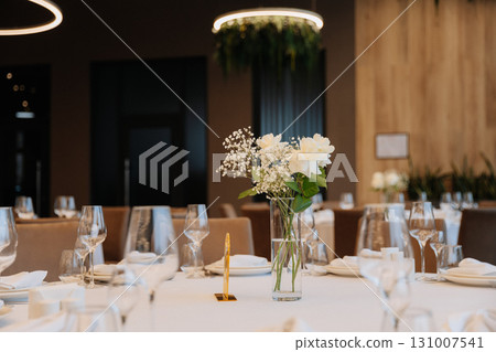 Elegant wedding table setup with white flowers and modern lighting in luxury restaurant 131007541
