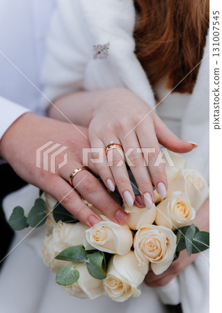 Wedding rings on bride and grooms hands over elegant bouquet of white roses Wedding rings on bride and grooms hands over elegant bouquet of white roses 131007545