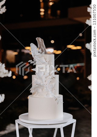 Elegant white wedding cake with sugar floral decor on modern stand at luxury reception Elegant white wedding cake with sugar floral decor on modern stand at luxury reception 131007550