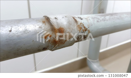 Rusty metal pipe showing wear in a modern indoor setting next to white walls Rusty metal pipe showing wear in a modern indoor setting next to white walls 131008047