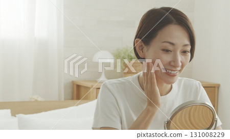 一位 40 多歲的日本女性對著鏡子檢查自己的皮膚狀況 131008229