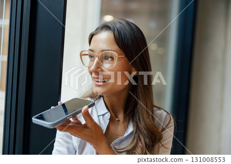 A Young Woman Engaged in Using Her Smartphone While Seated in a Modern Office Environment A Young Woman Engaged in Using Her Smartphone While Seated in a Modern Office Environment 131008553