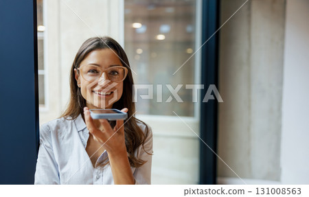 A confident woman engaging with her smartphone while in a modern office space setting A confident woman engaging with her smartphone while in a modern office space setting 131008563