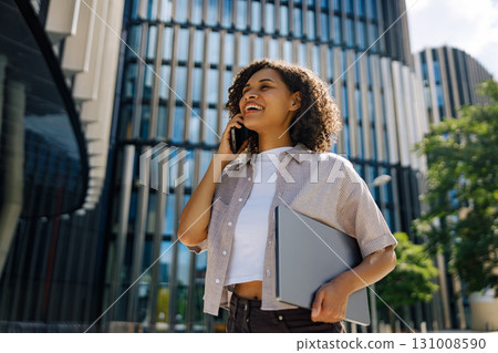 A confident businesswoman engaged in a phone conversation while surrounded by an urban setting 131008590