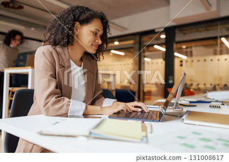A professional woman is diligently working on her laptop in a contemporary office environment A professional woman is diligently working on her laptop in a contemporary office environment 131008617