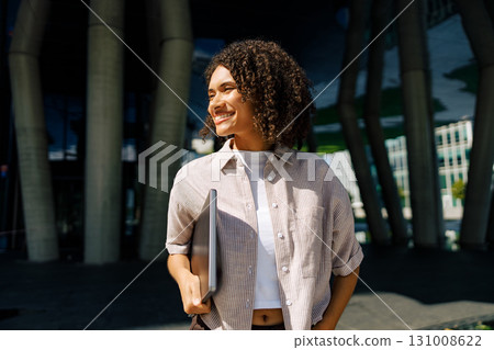 A Young Professional smiles outdoors, working on a laptop with confidence and positivity A Young Professional smiles outdoors, working on a laptop with confidence and positivity 131008622