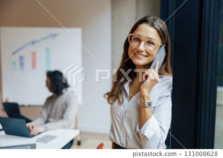 A Professional Woman Engaged in a Phone Conversation Within a Modern, Efficient Office Environment 131008628