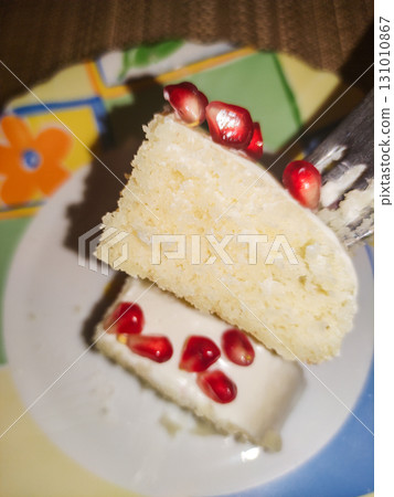 Fork lifting slice of vanilla cake with pomegranate seeds and white frosting for birthday Fork lifting slice of vanilla cake with pomegranate seeds and white frosting for birthday 131010867