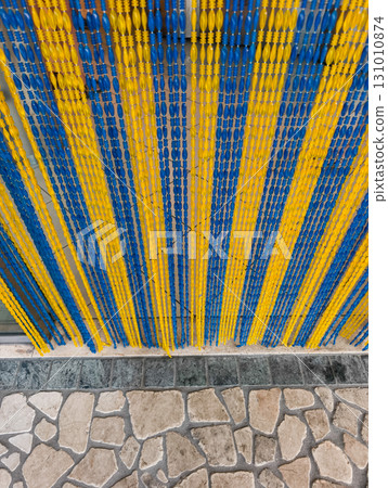 Blue and yellow beaded curtain hanging over stone floor in lignano sabbiadoro Blue and yellow beaded curtain hanging over stone floor in lignano sabbiadoro 131010874