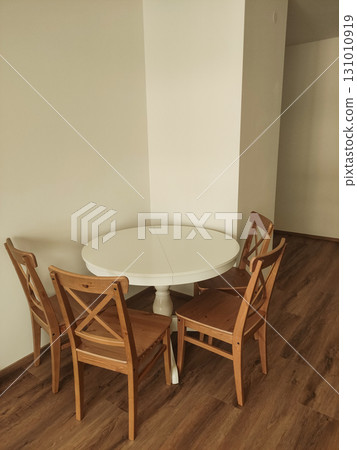 Round white table with four wooden chairs in a corner 131010919