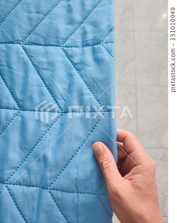 Hand touching soft blue quilted fabric in bathroom 131010949