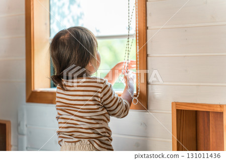 A girl playing with the roller blinds and pulling on the blinds cords, rear view 131011436