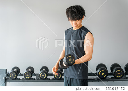 Young Asian man doing muscle training with dumbbells at the gym 131012452