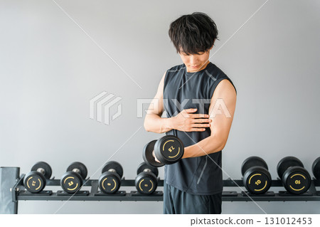 Young Asian man doing muscle training with dumbbells at the gym Young Asian man doing muscle training with dumbbells at the gym 131012453
