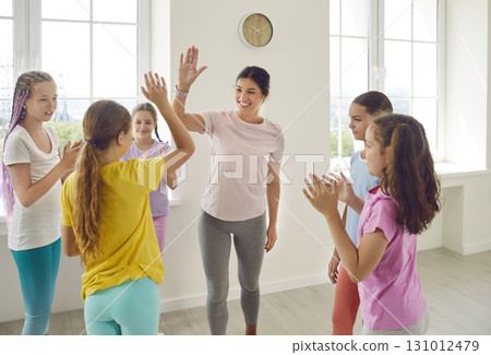 Happy dance sport trainer giving high five to her kids at the end of class in choreography studio. Happy dance sport trainer giving high five to her kids at the end of class in choreography studio. 131012479