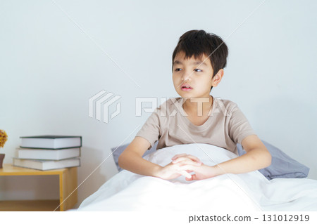 Asian boy wakes up in the early morning, feeling groggy and reluctant to leave the comfort of his bed. He yawns deeply, rubs his sleepy eyes, and stretches his arms and body lazily. Asian boy wakes up in the early morning, feeling groggy and reluctant to leave the comfort of his bed. He yawns deeply, rubs his sleepy eyes, and stretches his arms and body lazily. 131012919