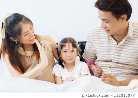 Happy Asian family with father, pregnant mother, and daughter are relaxing or lying down on the bed and talking together. A concept of happiness in family. 131013077
