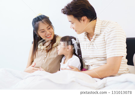 Happy Asian family with father, pregnant mother, and daughter are relaxing or lying down on the bed and talking together. A concept of happiness in family. 131013078