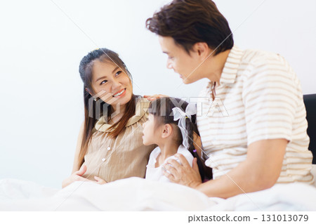 Happy Asian family with father, pregnant mother, and daughter are relaxing or lying down on the bed and talking together. A concept of happiness in family. 131013079