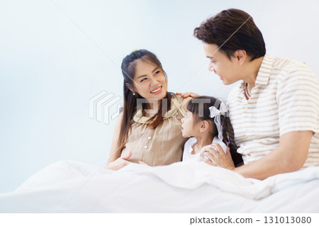 Happy Asian family with father, pregnant mother, and daughter are relaxing or lying down on the bed and talking together. A concept of happiness in family. 131013080