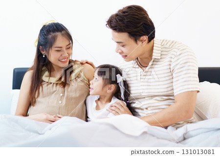 Happy Asian family with father, pregnant mother, and daughter are relaxing or lying down on the bed and talking together. A concept of happiness in family. Happy Asian family with father, pregnant mother, and daughter are relaxing or lying down on the bed and talking together. A concept of happiness in family. 131013081