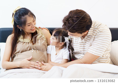 Happy Asian family with father, pregnant mother, and daughter are relaxing or lying down on the bed and talking together. A concept of happiness in family. 131013082