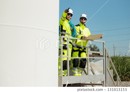 Team of professional electrical engineers in fully safety suit are working and discussing together at the windmill electric generating turbine. Electricians working at the site of windmill turbine. 131013153