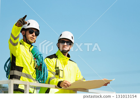 Team of professional electrical engineers in fully safety suit are working and discussing together at the windmill electric generating turbine. Electricians working at the site of windmill turbine. 131013154