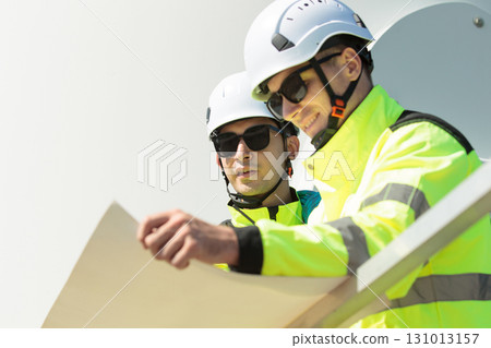 Team of professional electrical engineers in fully safety suit are working and discussing together at the windmill electric generating turbine. Electricians working at the site of windmill turbine. 131013157