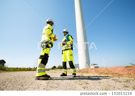 Team of professional electrical engineers in fully safety suit are working and discussing together at the windmill electric generating turbine. Electricians working at the site of windmill turbine. 131013158