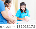 An Asian husband and his pregnant wife are learning how to bathe a newborn baby, guided by a nanny nurse who is demonstrating the bathing process using a baby doll. 131013178