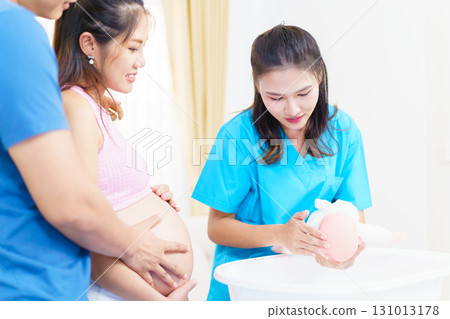 An Asian husband and his pregnant wife are learning how to bathe a newborn baby, guided by a nanny nurse who is demonstrating the bathing process using a baby doll. An Asian husband and his pregnant wife are learning how to bathe a newborn baby, guided by a nanny nurse who is demonstrating the bathing process using a baby doll. 131013178