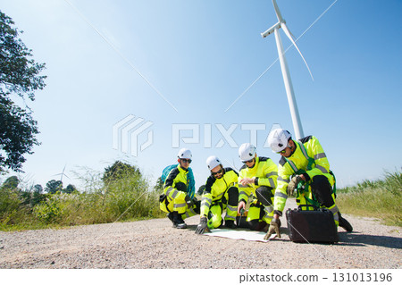 Team of professional electrical engineers in fully safety suit are working and discussing together at the windmill electric generating turbine. Electricians working at the site of windmill turbine. Team of professional electrical engineers in fully safety suit are working and discussing together at the windmill electric generating turbine. Electricians working at the site of windmill turbine. 131013196