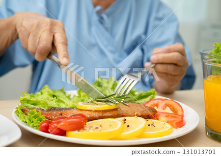 Asian elderly woman patient eating salmon stake and vegetable salad for healthy food in hospital. 131013701