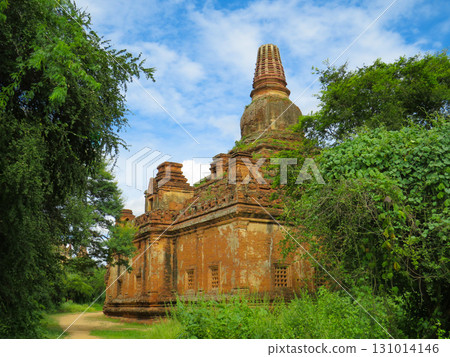 A large Buddhist temple of re brick seen behind grfeen trees 131014146