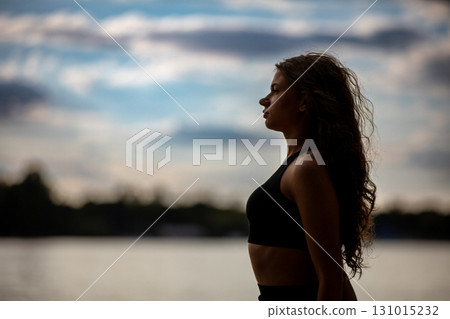 Silhouette of a Confident Woman Standing Gracefully by the Water at Sunset, Capturing Strength 131015232