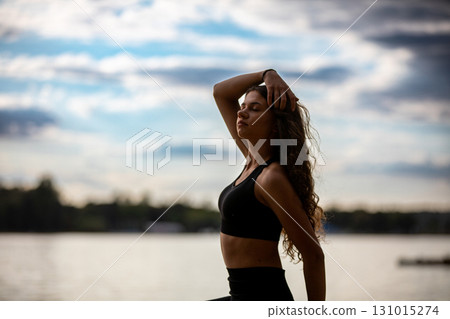 Engaging in a Dynamic Yoga Pose by the tranquil Water, surrounded by natures beauty Engaging in a Dynamic Yoga Pose by the tranquil Water, surrounded by natures beauty 131015274