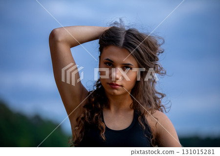 A Young Woman with Beautiful Curly Hair Posing Outdoors in the Soft Light of the Golden Hour A Young Woman with Beautiful Curly Hair Posing Outdoors in the Soft Light of the Golden Hour 131015281