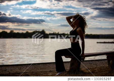 A Woman Relaxing Outdoors by the Peaceful Water During Dusk, Surrounded by Natures Beauty 131015297