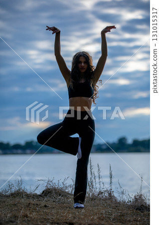 A Dancer Beautifully Posing Gracefully by the Water during a Stunning Sunset Scene 131015317