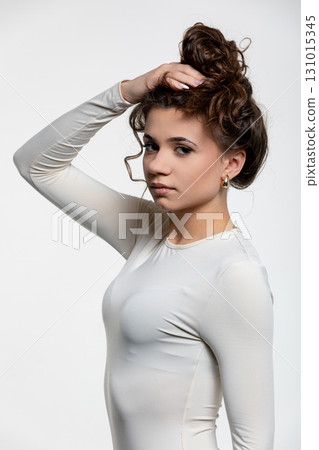 A Young Girl Dressed in a Beautiful White Dress with Curly Hair Posing Elegantly 131015345