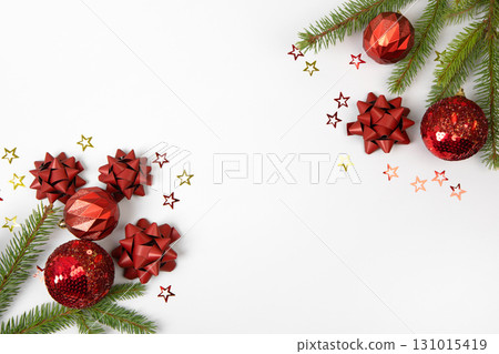 Christmas card made of green Christmas tree branches, red decorative balls, red bows, and glitter stars on gray background with space for text and greetings. Flat lay, copy space 131015419