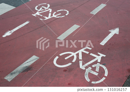 Red painted bike lane with clear white symbols indicating direction of travel for cyclists, promoting cycling as sustainable and safe means of urban mobility, modern infrastructure 131016257