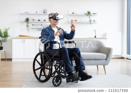 Older man in wheelchair experiencing virtual reality using VR headset, engaging in physical gesture-based interaction in a modern, bright indoor setting. Older man in wheelchair experiencing virtual reality using VR headset, engaging in physical gesture-based interaction in a modern, bright indoor setting. 131017398