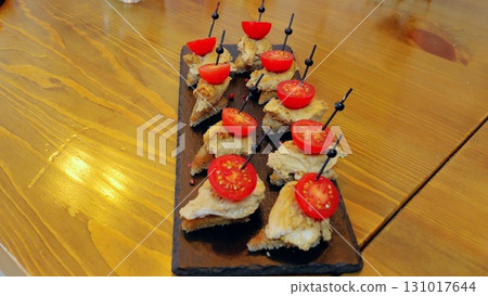 Gourmet bruschetta with grilled chicken and cherry tomatoes plated on dark slate, presenting sophisticated culinary styling 131017644