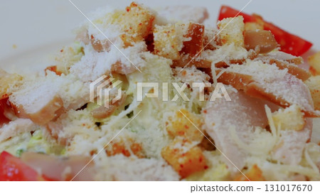 Fresh caesar salad presenting grilled chicken strips, crispy croutons, shredded parmesan, ripe tomato slices arranged appetizingly on white ceramic plate 131017670