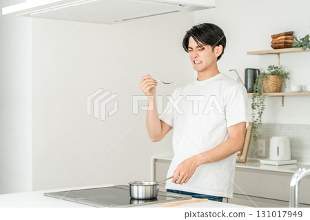 A young Asian man cooking and tasting food in the kitchen (bad taste, failure) 131017949