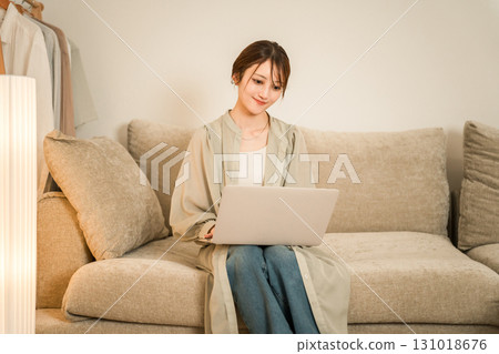 A young Asian woman sitting on a sofa in the living room at night and looking at a laptop A young Asian woman sitting on a sofa in the living room at night and looking at a laptop 131018676